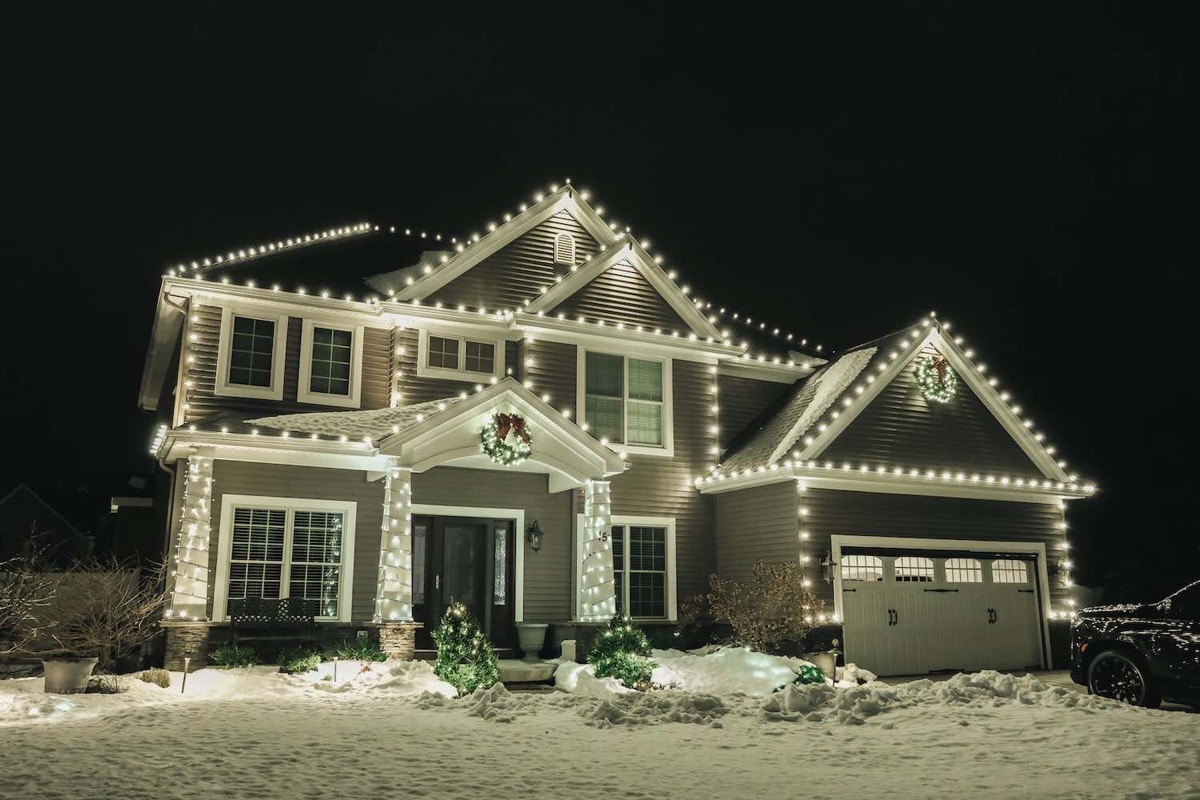 A home on a snowy night with warm-white roofline lights and porch columns wrapped in lights.
